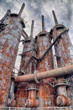 an old factory with rusty pipes and rusted paint on it's walls, against a cloudy sky