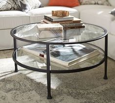 a glass table with books on it in front of a couch and coffee table next to pillows