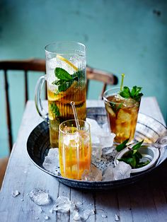 three glasses filled with drinks on top of a metal tray next to ice cubes