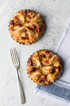 two small pies sitting on top of a table next to a fork and napkin