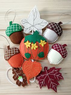 an assortment of felt ornaments hanging from strings on a wooden surface with leaves and acorns