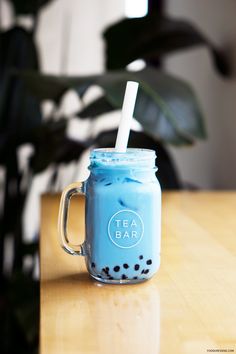 a blue mason jar with a straw in it sitting on a table next to a potted plant