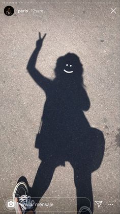 a shadow of a person with a hand up in the air and a smiley face drawn on the ground