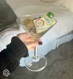 a person holding up a martini glass in front of a bed