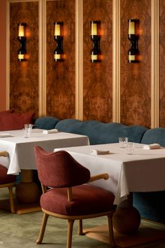 two tables with white tablecloths and red chairs in front of wood paneled walls