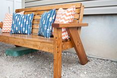 a wooden bench with three pillows on it sitting in front of a building and door