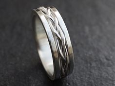 a silver ring with two braiding lines on the inside of it, sitting on a black surface