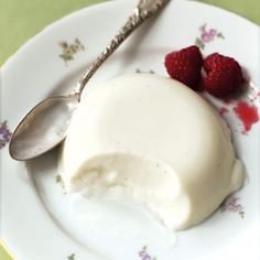 a white plate topped with ice cream and two raspberries next to a spoon