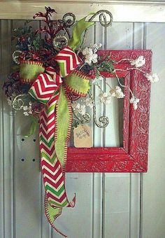 a red and green wreath hanging on the front door with a bow attached to it