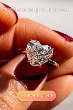 a woman's hand holding an engagement ring with a heart shaped diamond on it