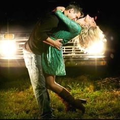 a man and woman kissing in front of a truck at night with the lights on