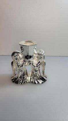 a silver vase sitting on top of a table next to a white wall and floor