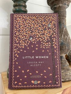 a little women book sitting on top of a wooden table next to two vases