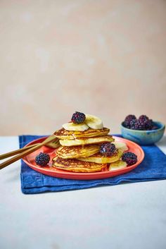 pancakes with berries and maple syrup on a red plate next to some chopsticks