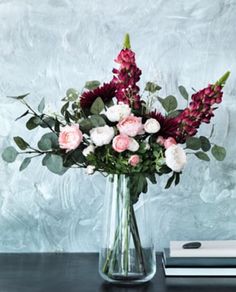 a vase filled with pink and white flowers on top of a table next to a book