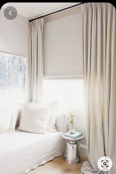 a white bed sitting in a bedroom next to a window with drapes on it