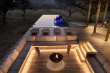 an outdoor living area with couches and tables lit up at night, overlooking a pool