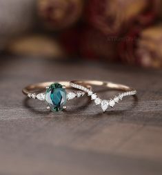 two gold rings with green and white stones on them sitting on top of a wooden table