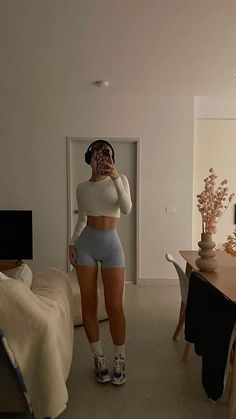 a woman is taking a selfie in her living room wearing high waist shorts and white crop top