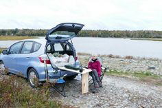 a woman sitting at a picnic table next to a car with its trunk open and it's hatch opened