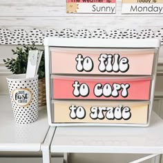 a white desk topped with a pink and yellow dresser next to a cup filled with coffee