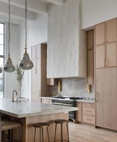 a kitchen with wooden cabinets and marble counter tops, two pendant lights hanging over the island