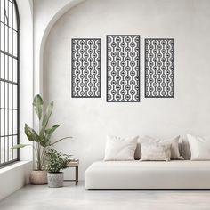 a white couch sitting in front of a window next to two paintings on the wall