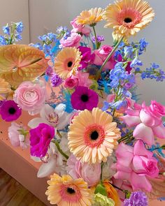 a bouquet of colorful flowers sitting on top of a wooden table next to a mirror