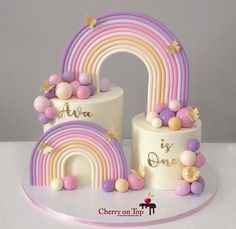 two tiered cake with rainbow decorations on top, and the word ava is one above it