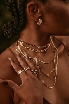 a woman with multiple necklaces and rings on her neck, holding her hands to her chest