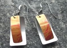 pair of earrings with orange and red designs on them sitting on top of a granite surface