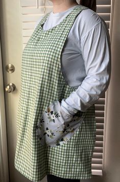 a woman standing in front of a door wearing a green and white apron with flowers on it