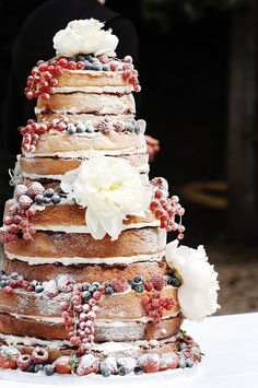 a wedding cake with flowers and berries on it's tiered tower is ready to be cut