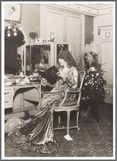 an old black and white photo of a woman sitting in a chair reading a book