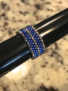 a black pen with blue and silver beads on it's end sitting on a marble surface