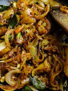 stir fry with onions and spinach in a wok on the table next to a wooden spoon