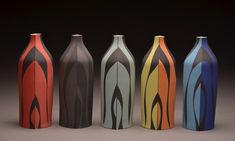 five different colored vases sitting side by side on a black background, each with an abstract design