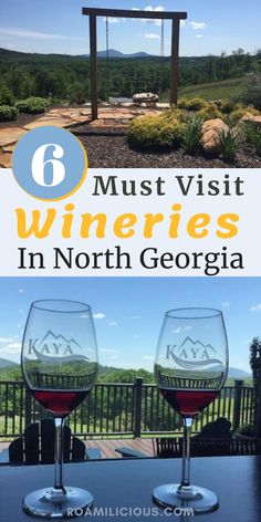 two wine glasses sitting on top of a wooden table next to a gazebo with mountains in the background