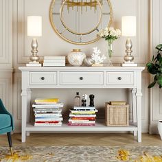 a white table topped with lots of books next to a blue chair and a mirror