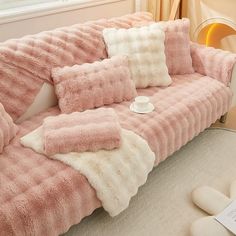 a pink couch with two pillows and a cup on the table in front of it