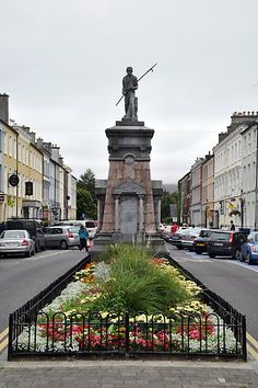 a statue in the middle of a street with flowers and plants growing out of it