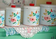 four canisters with flowers painted on them are sitting on a shelf in the kitchen