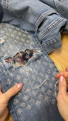 two hands are working on an old pair of jeans that have been torn and stitched together