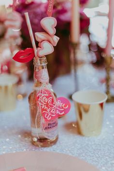 a bottle filled with candy hearts sitting on top of a table next to a cup