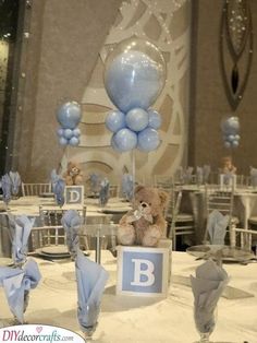 a teddy bear sitting on top of a table next to blue and white balloons in the shape of letters