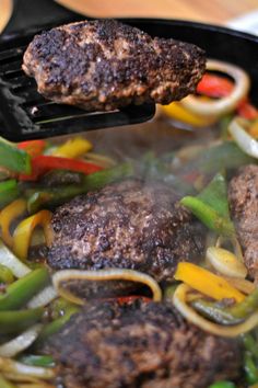 a hamburger being cooked in a skillet with peppers and onions on the side,