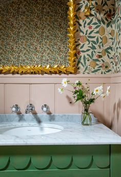 a bathroom sink with flowers in a vase on the counter and a mirror above it