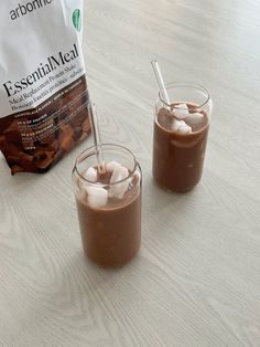 two glasses filled with ice cream sitting on top of a table next to a bag of chocolate