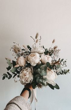 a woman holding a bouquet of flowers in her hand with white and green foliage on it