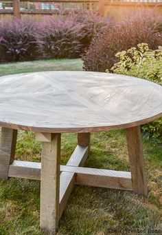 a wooden table sitting on top of a grass covered field next to bushes and flowers